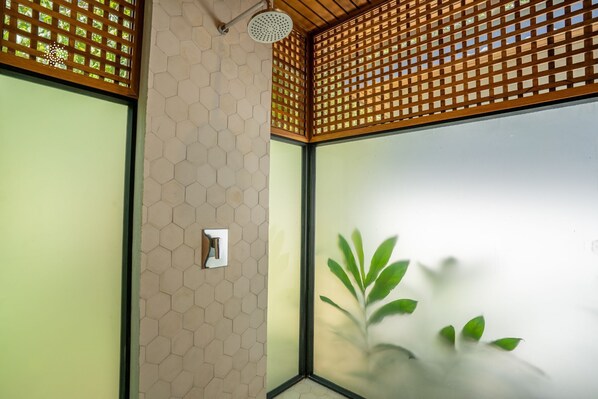 Une pièce avec un mur recouvert de carreaux hexagonaux, un plafond en treillis de bois et une grande fenêtre ornée d’une plante.