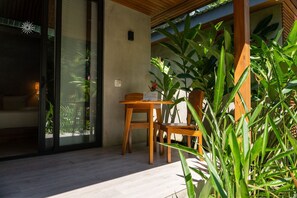 A modern outdoor seating area with a wooden table and chairs, surrounded by lush green plants. - Serenity Bungalows Beach & Jungle Escape + AC (Puerto Viejo de Talamanca)