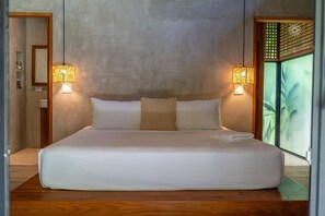A large bed with two bedside lamps, a wooden floor, and a view of greenery through a sliding door. - Serenity Bungalows Beach & Jungle Escape + AC (Puerto Viejo de Talamanca)