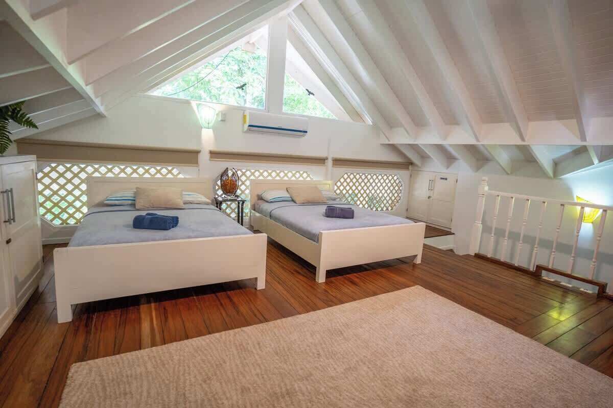 A bedroom with two beds, a wooden floor, a white ceiling, and a window.