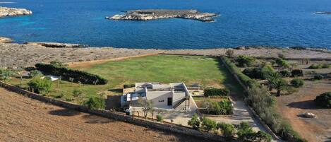 A coastal property with a large lawn, a modern house, and rocky outcrops in the sea.