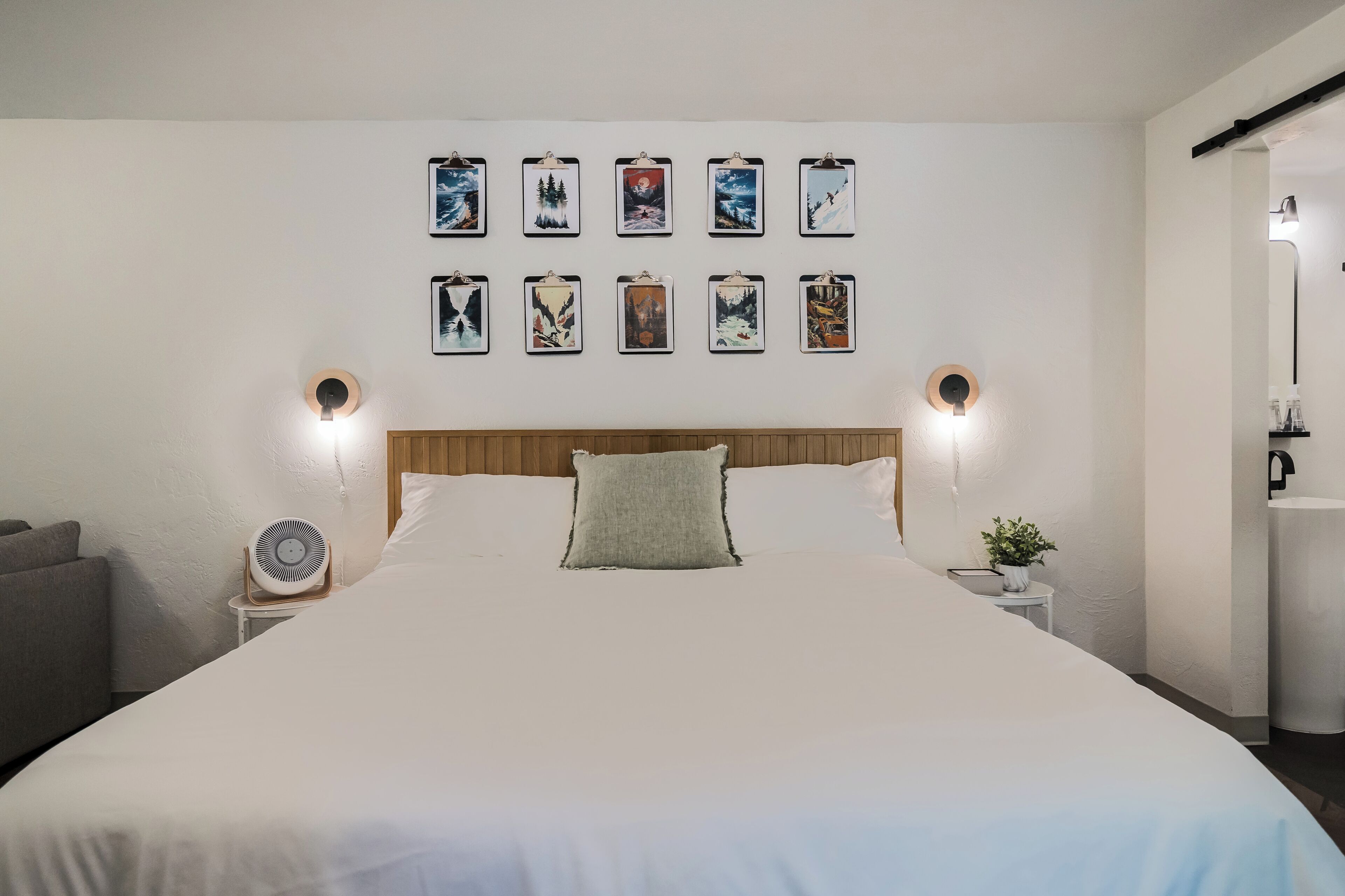 A neatly made bed with a wooden headboard, a bedside table with a lamp, and a wall decorated with framed pictures.