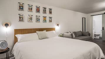 Ein Schlafzimmer mit einem großen Bett, einem Holzkopfteil, einer grauen Couch und einer Wandleuchte.