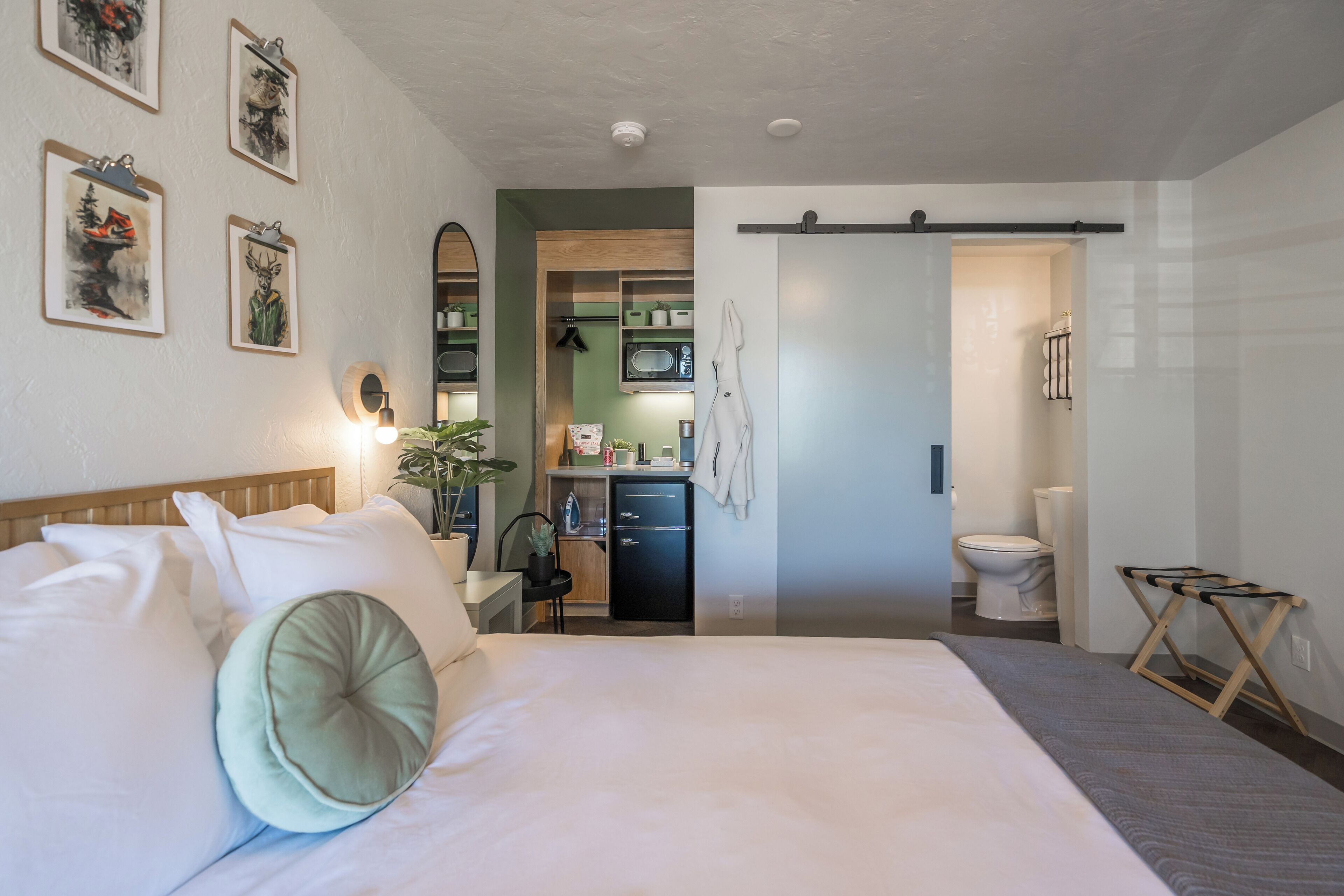 Habitación de hotel con una cama grande, un escritorio con silla, una kitchenette pequeña y un baño.