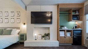 A modern bedroom with a large bed, a flat-screen TV mounted above a fireplace, and a kitchenette area with a microwave and refrigerator. - The Local Motel & Shops (Eugene)