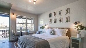 A modern bedroom with a large bed, bedside tables, a small table with chairs, and a balcony with a railing. - The Local Motel & Shops (Eugene)