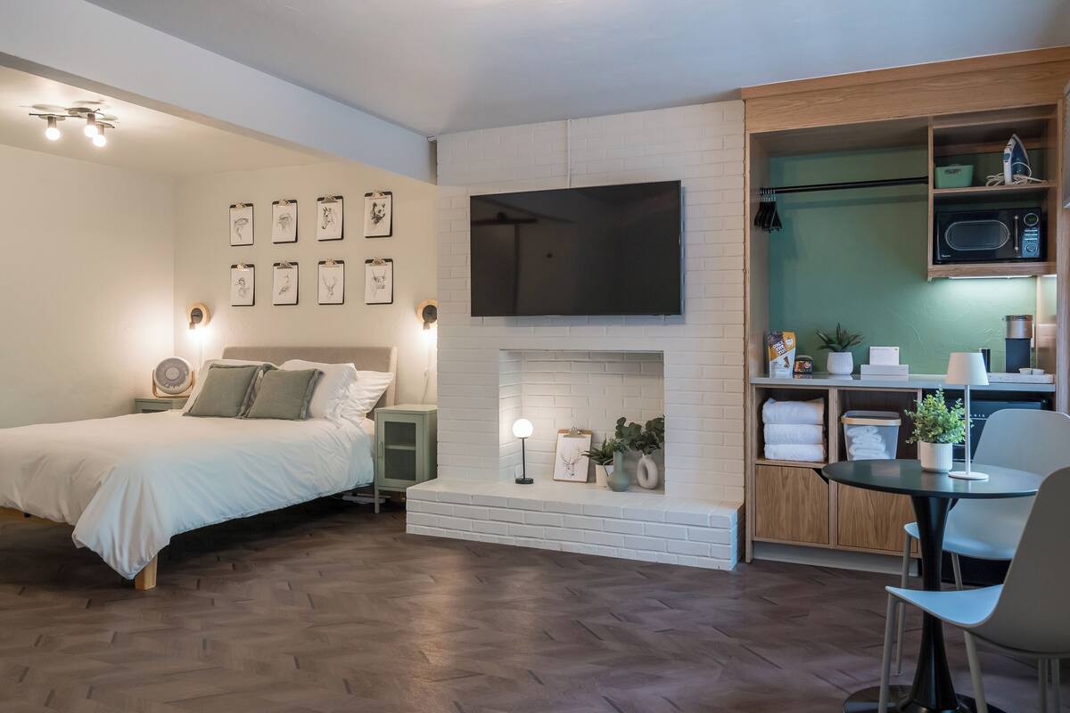 A modern bedroom with a bed, bedside tables, a flat-screen TV, and a small dining area with a table and chairs.