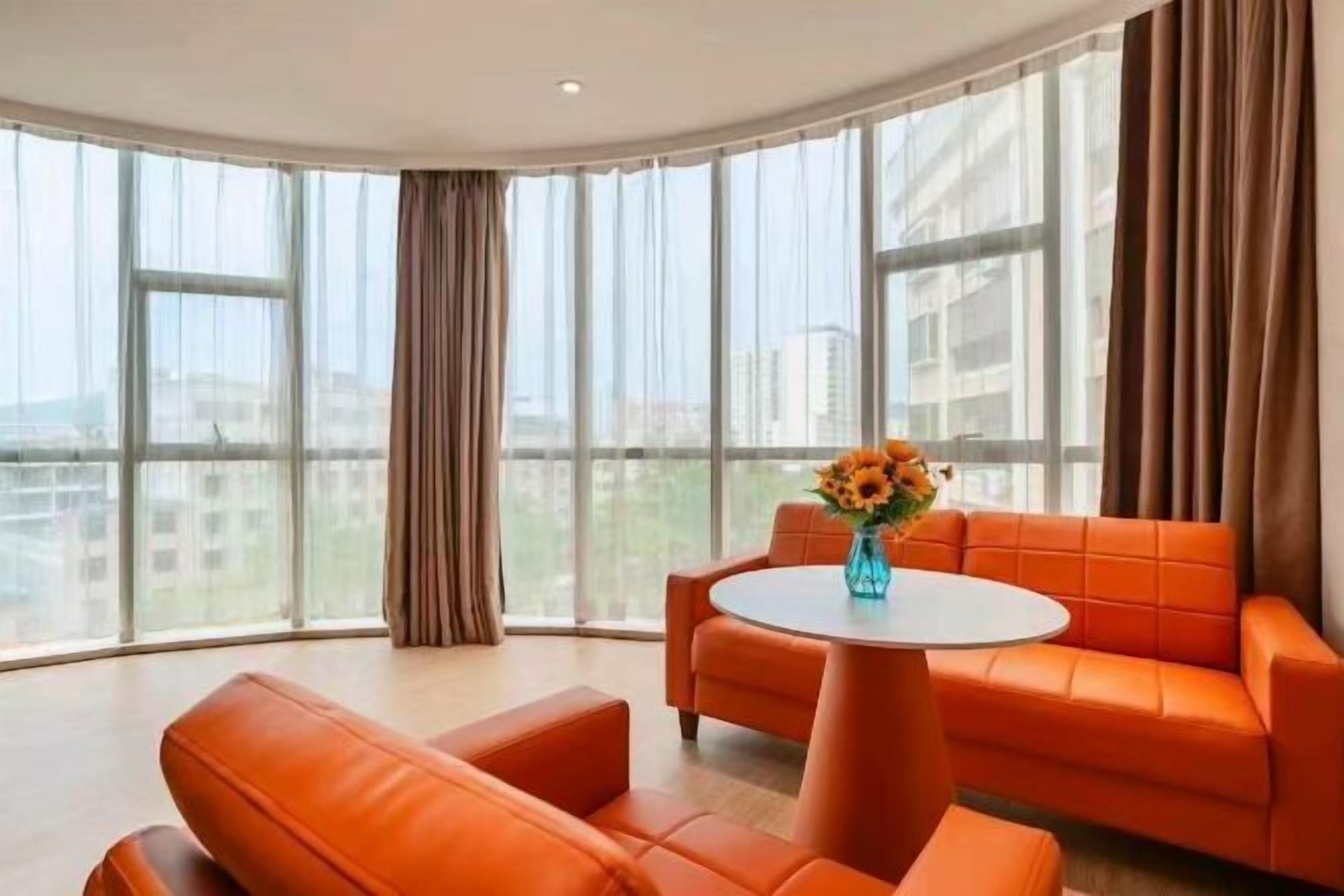 A modern room with a curved ceiling, a round table, orange leather sofas, and a large window with curtains.