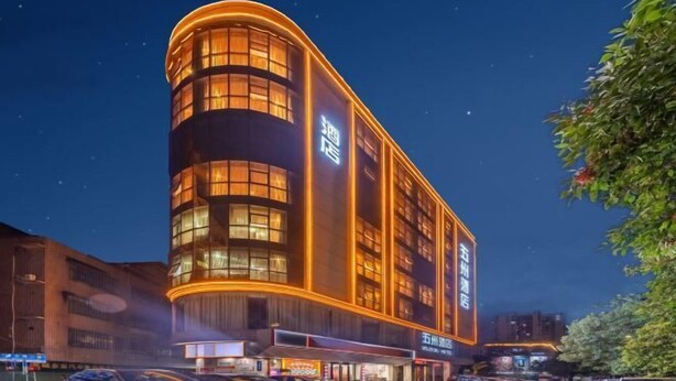 Een modern hotel met een gebogen gevel, verlichte ramen en een bord dat aangeeft dat het een hotel is.