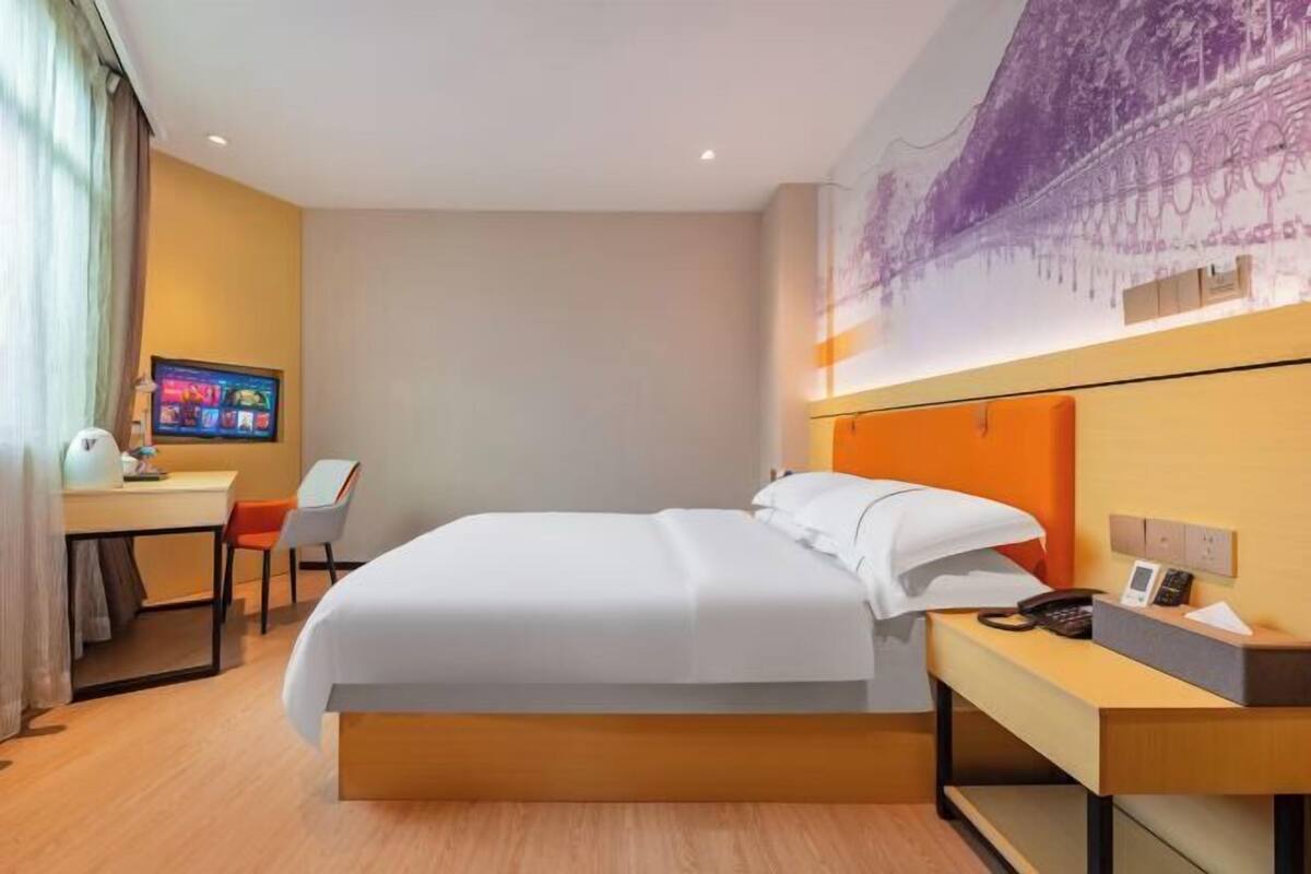 Habitación de hotel con cama, escritorio con computadora, silla y televisor montado en la pared.