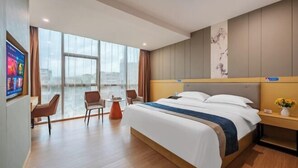 Een moderne hotelkamer met een groot bed, een bureau en een stoel. Een groot raam biedt uitzicht op de stad.