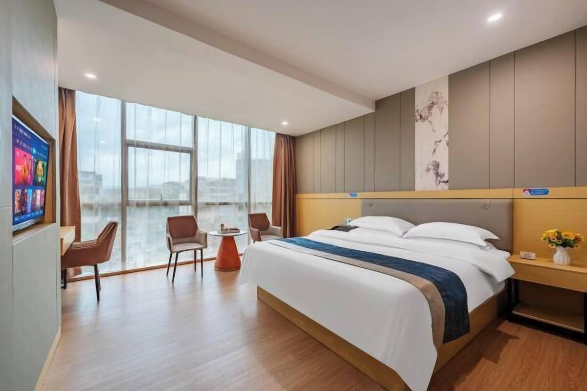 Una habitación de hotel moderna con una cama grande, un escritorio y una silla. Hay un ventanal con vistas a la ciudad.