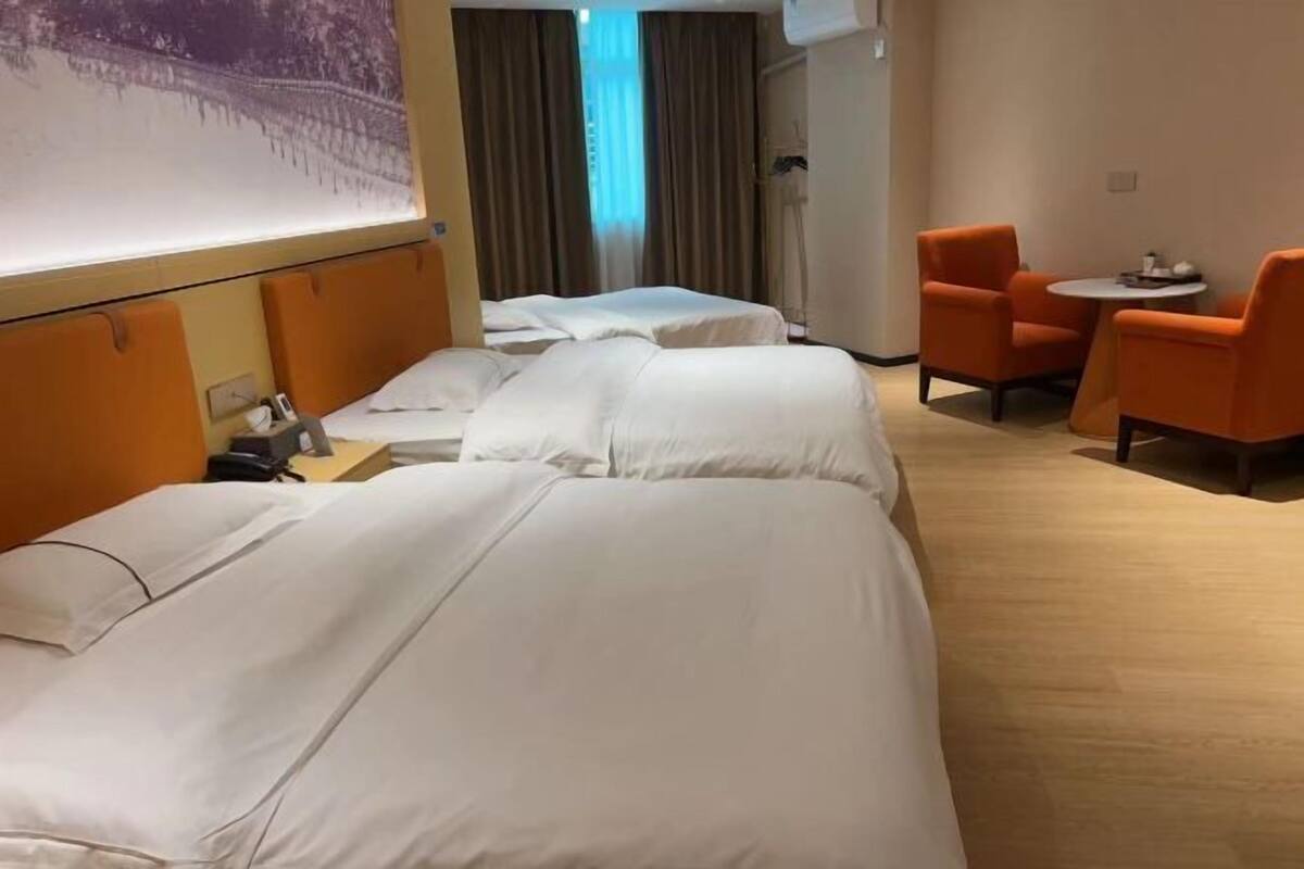 Habitación de hotel con dos camas, una mesita con sillas y un ventanal con cortinas.