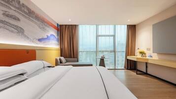 Habitación de hotel con una cama grande, un escritorio, una silla y vistas a la ciudad a través de amplias ventanas.