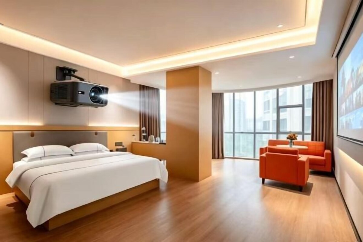 Ein modernes Hotelzimmer mit einem großen Bett, einer Sitzecke, einem Projektor und einem großen Fenster.