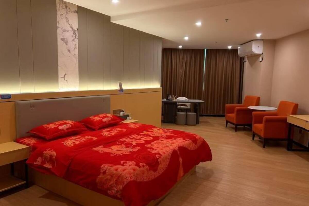Habitación de hotel con una cama grande, un escritorio, dos sillas, una mesita y aire acondicionado instalado en la pared.