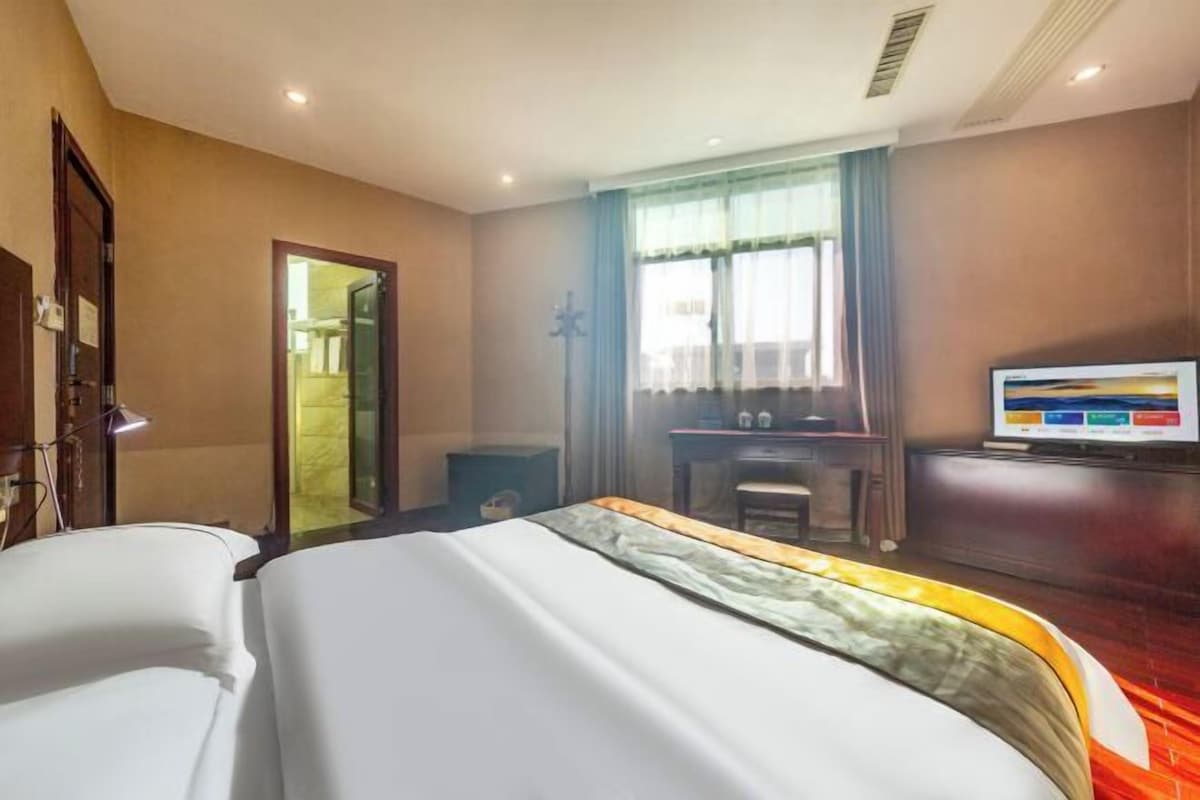A hotel room with a bed, a desk, a television, and a window with curtains.