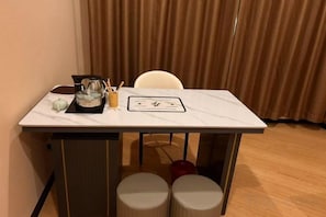 A small dining table with a white marble top, a coffee pot, a cup, and a menu. There are two stools and a chair.