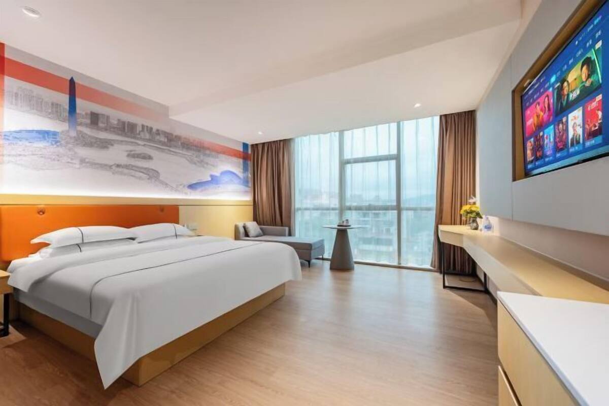 Habitación de hotel moderna con una cama grande, un escritorio, una silla y un televisor montado en la pared.