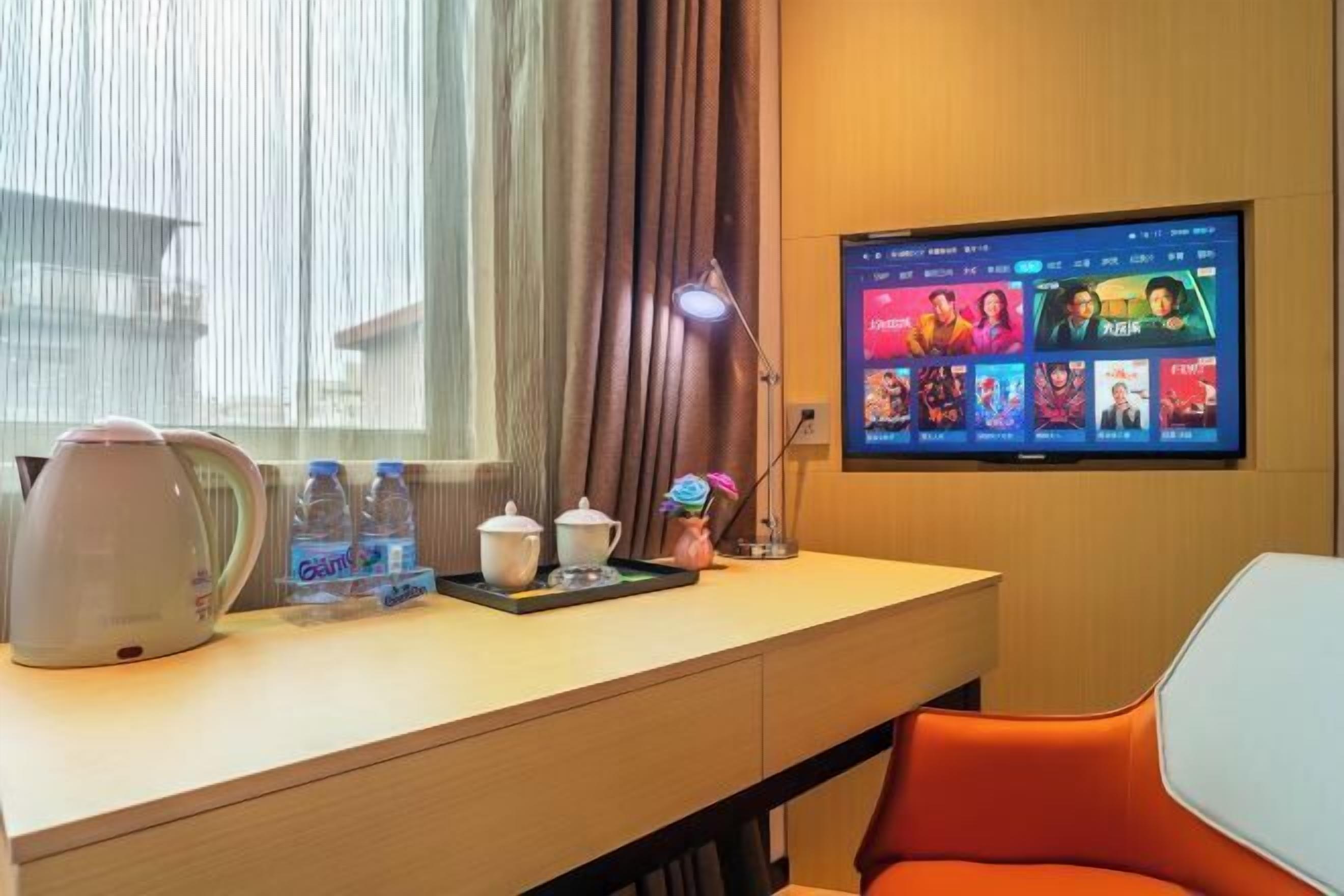 Ein Hotelzimmer mit Schreibtisch, einem Flachbildfernseher, der eine Auswahl an Filmen zeigt, einem Wasserkocher und Wasserflaschen.