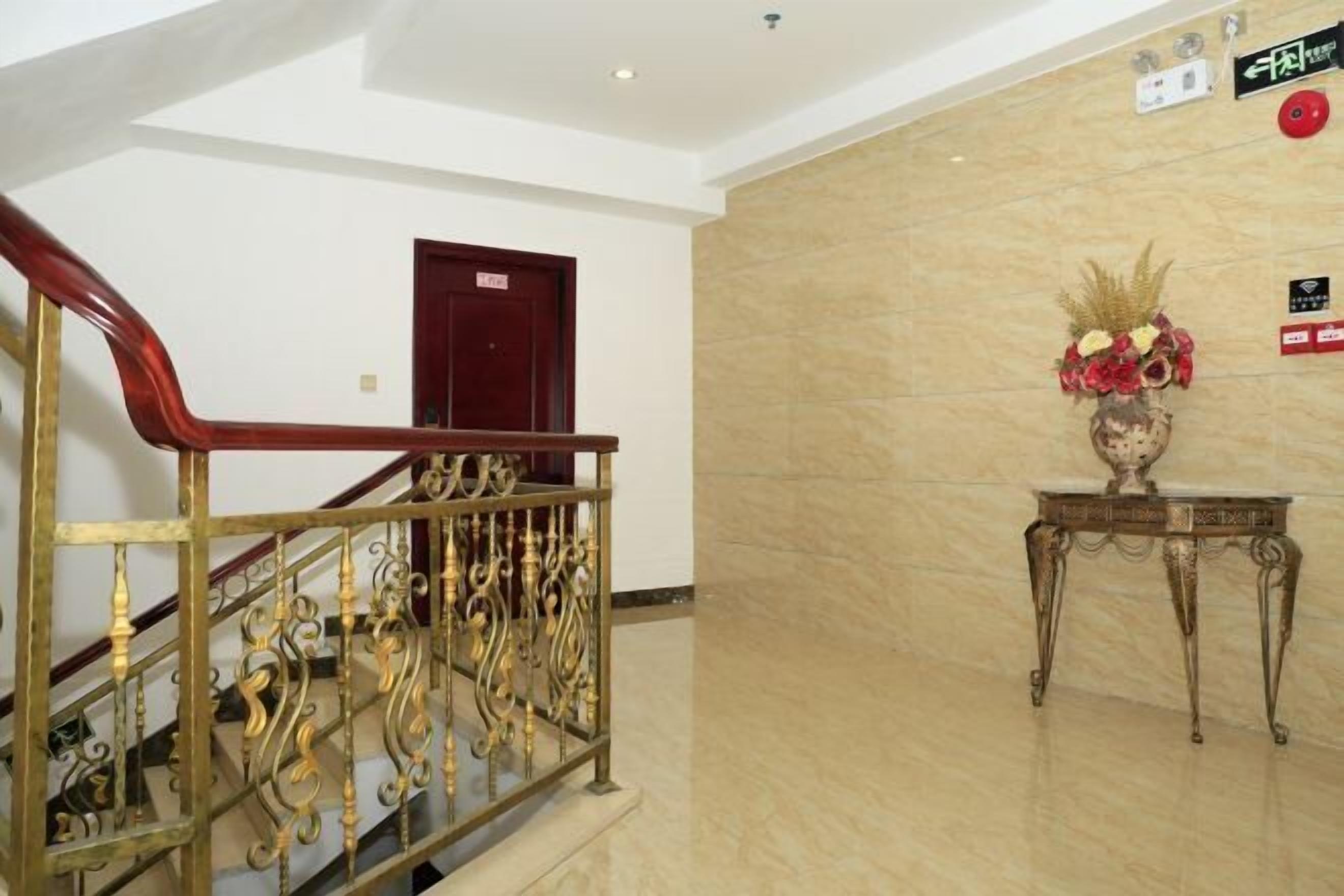 A marble-floored lobby with a staircase featuring ornate golden railings and a red door in the background.