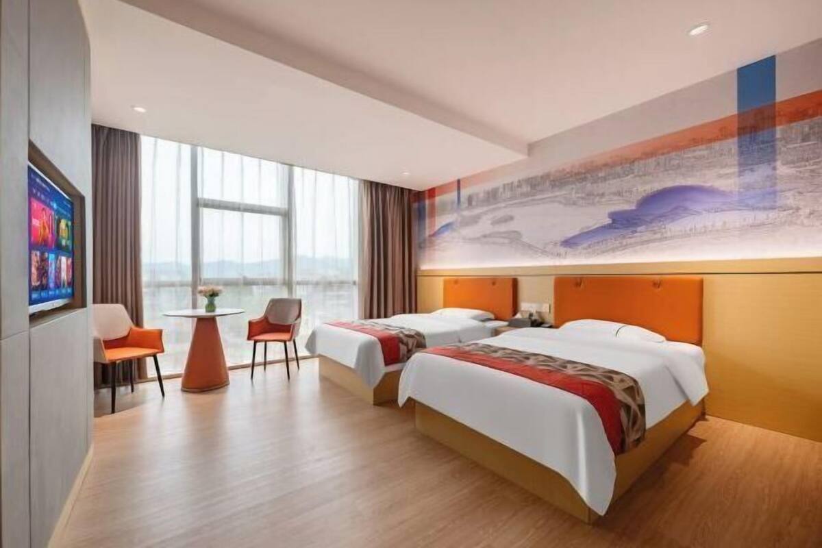 Habitación de hotel con dos camas, una mesita pequeña y un televisor.