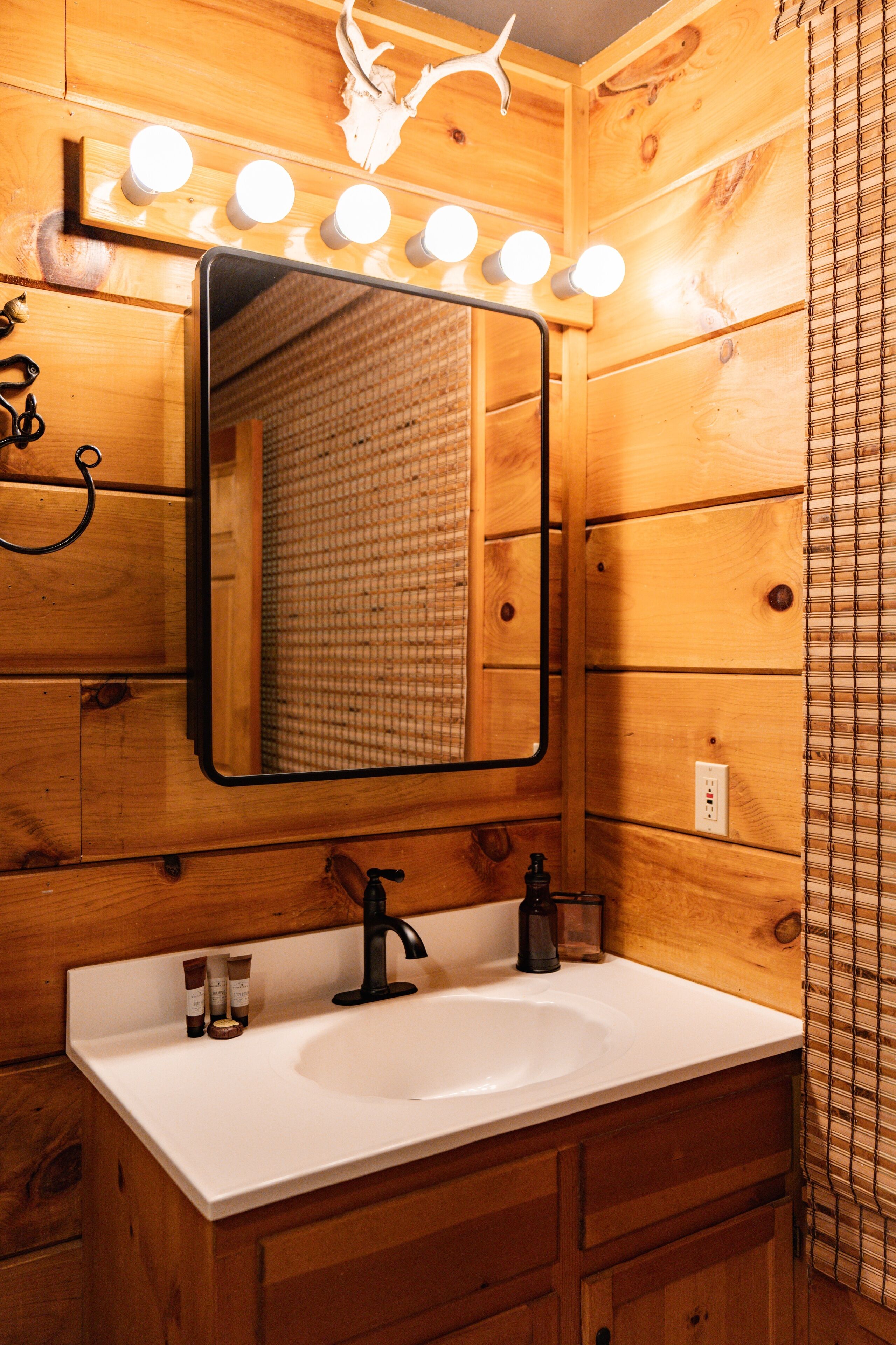 Ein Badezimmer aus Holz mit einem weißen Waschbecken, einem Spiegel und einem beleuchteten Waschtisch.