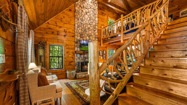 Ein Holzblockhaus-Interieur mit Kamin aus Stein, einer Holztreppe und einer gemütlichen Sitzecke.