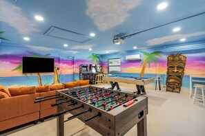 Ein Raum mit Tischfußball, Billardtisch und großem Fernsehbildschirm.