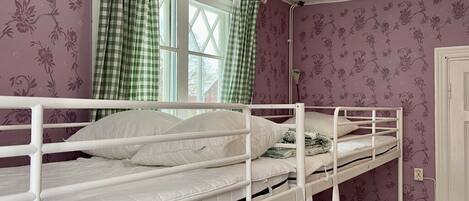 A bunk bed room with floral wallpaper, a window with checkered curtains, and a lamp on the floor.