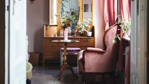 A room with a wooden dresser, a mirror, a pink chair, and a vase with flowers. - Herrgård de luxe (Tävelsås)