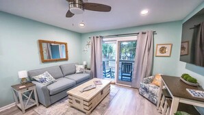 A living room with a grey sofa, a wooden coffee table, a small side table, and a dining area with a table and chairs. - Coligny Beachfront Villa w/Pool at The Breakers (Hilton Head Island)