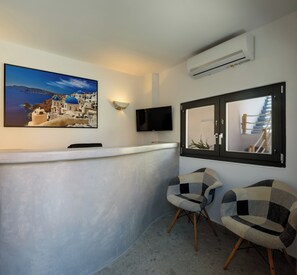 Une chambre moderne avec un grand tableau représentant un paysage côtier, un téléviseur à écran plat et deux fauteuils à motifs.