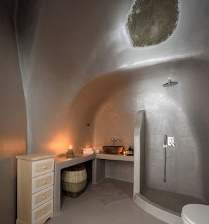 A modern bathroom with a unique curved ceiling, a wooden basin, a shower, and a small wooden cabinet with drawers. - White Dream Suites (Santorini)