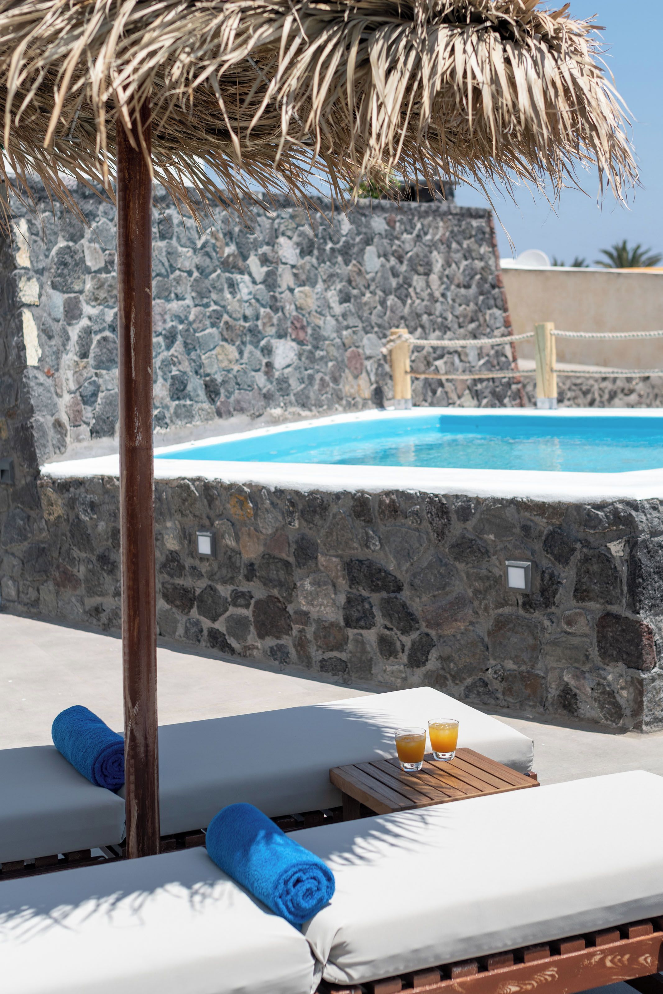 A poolside area with lounge chairs, a thatched umbrella, and a stone wall.