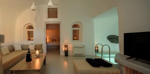 Una sala de estar moderna con un sofá, una mesa de centro con una botella y vasos, un televisor y vistas a una piscina.