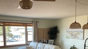 Een moderne woonkamer met een witte bank, een houten salontafel, een keukeneiland en een plafondventilator.