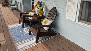 Een overdekt terras met houten meubilair, een gele bloempot en een blauw-witte vloerkleden.