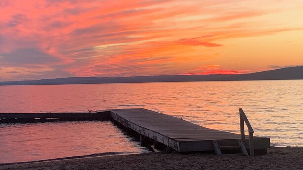 Een zonsondergang boven een kalm wateroppervlak, met een houten steiger die het water in reikt.