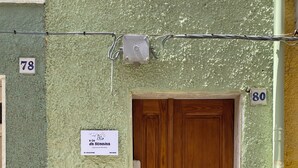 A wooden double door with a small window above it, set in a textured green wall with apartment numbers 78 and 80 visible. - At Granny's (Carloforte)