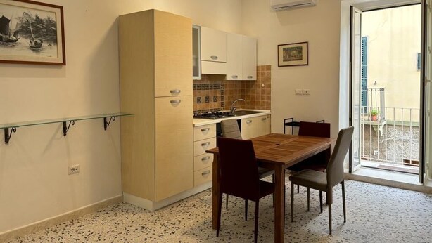 A compact kitchen with a dining area, a small balcony, and a framed picture on the wall. - At Granny's (Carloforte)