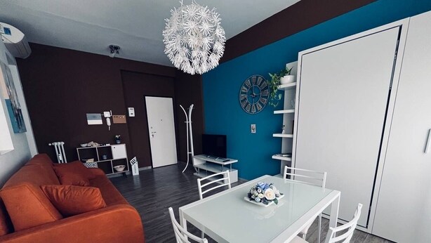 Una sala de estar moderna con un sofá, una mesa de comedor con sillas, una lámpara de techo blanca y un reloj en la pared.