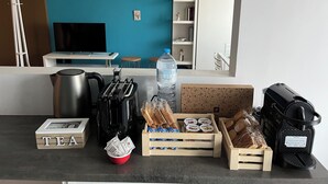 Una encimera de cocina con cafetera, tostadora, caja de té, botella de agua, pan y panera.