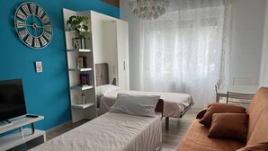 Un dormitorio con dos camas individuales, un sofá, un televisor y una estantería.