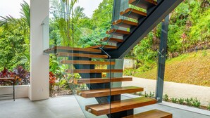 Un escalier moderne avec des rampes en verre et des marches en bois, entouré d’une végétation luxuriante.