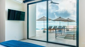 Une chambre d’hôtel moderne dotée d’une grande porte-fenêtre coulissante donnant sur un balcon avec coin salon extérieur et vue sur la mer.