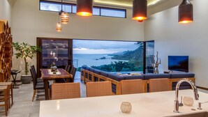 A modern dining area with a large island, wicker furniture, and a view of the sea. - Casa Ola Vista by Pura Villas (Dominical)
