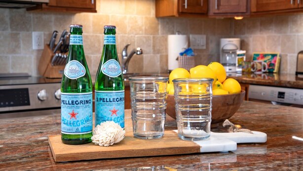 Un comptoir de cuisine avec des bouteilles d’eau minérale pétillante Pellegrino, un bol de citrons et une planche à découper en bois.
