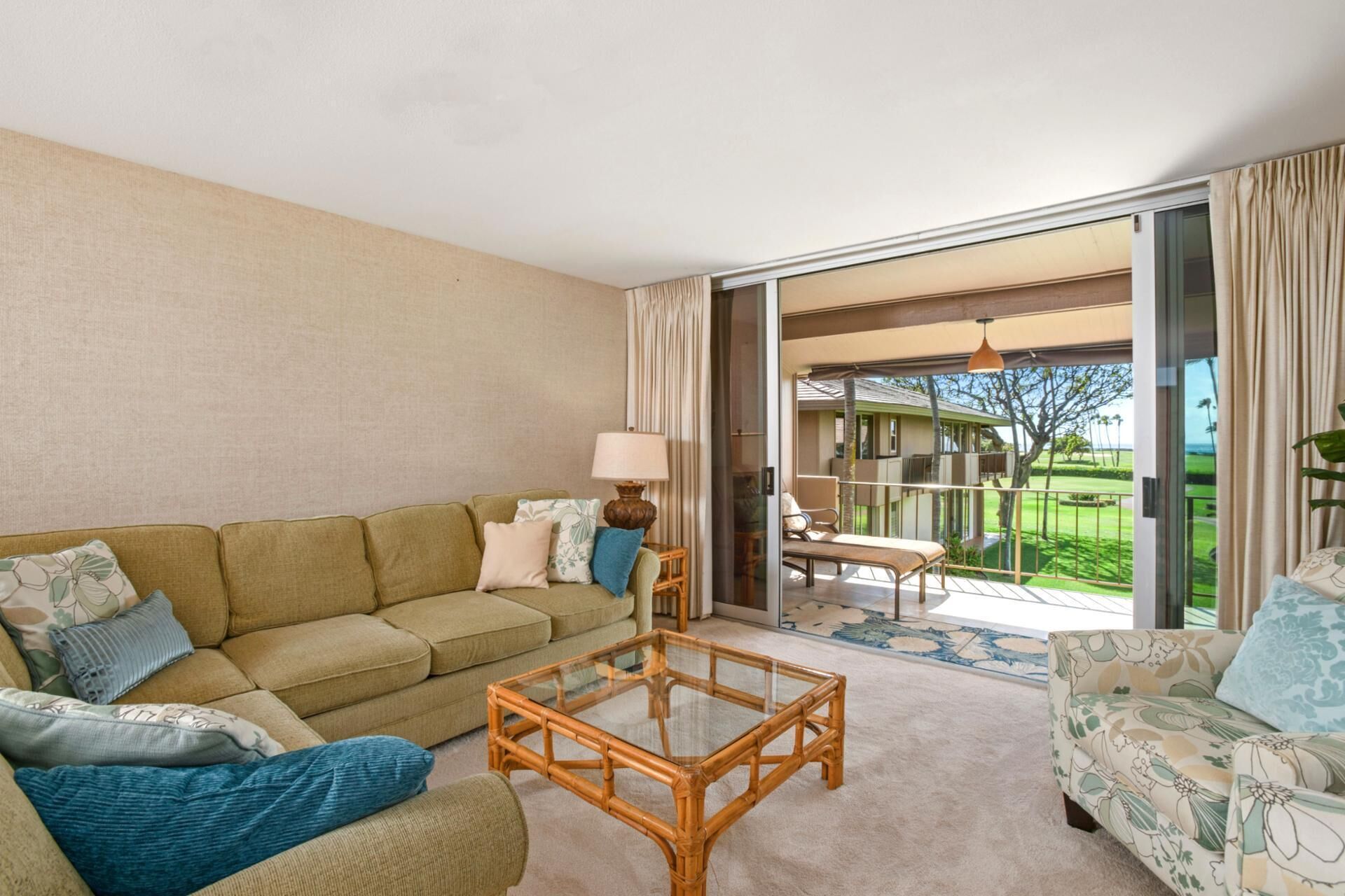 A living room with a sofa, a glass coffee table, and a view of a golf course through large sliding doors.