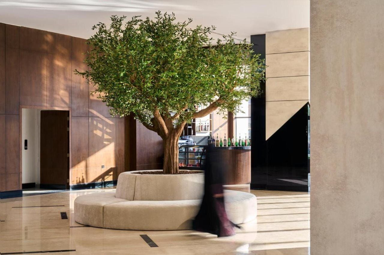 A modern lobby with a large tree, a curved seating area, and a staircase.